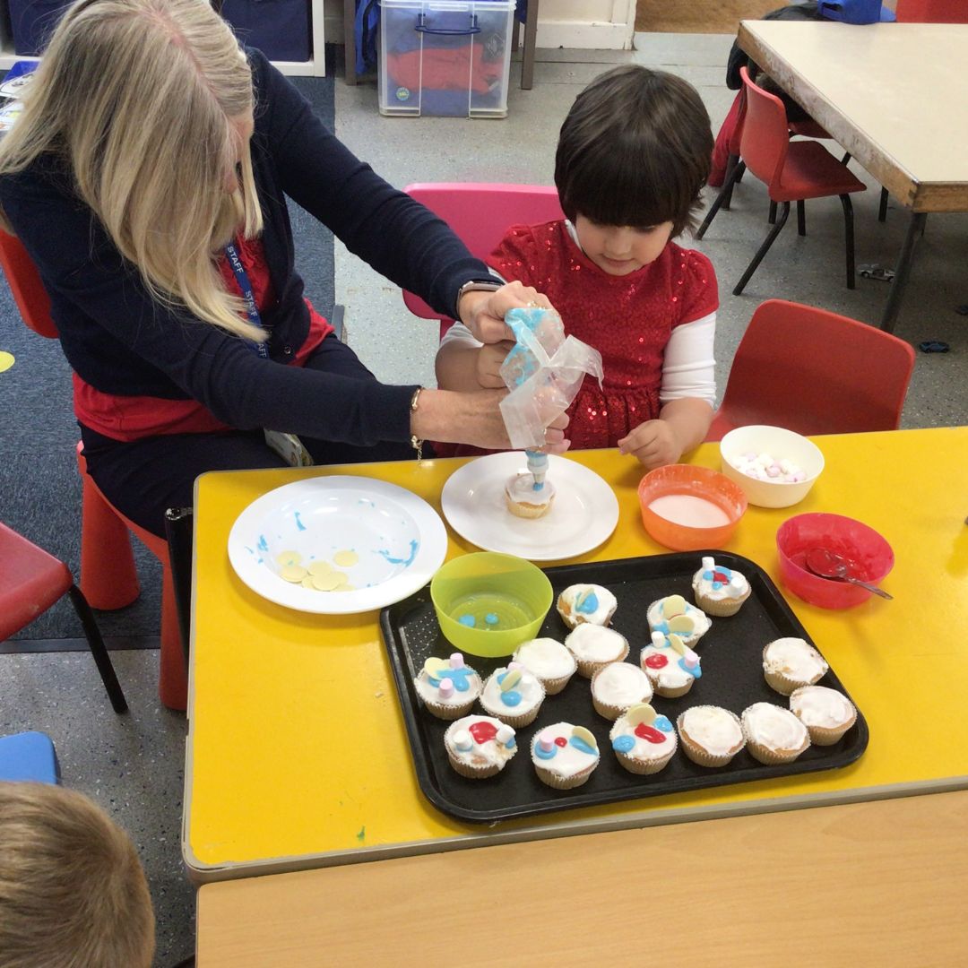 A nursery child icing cakes with help from a staff member