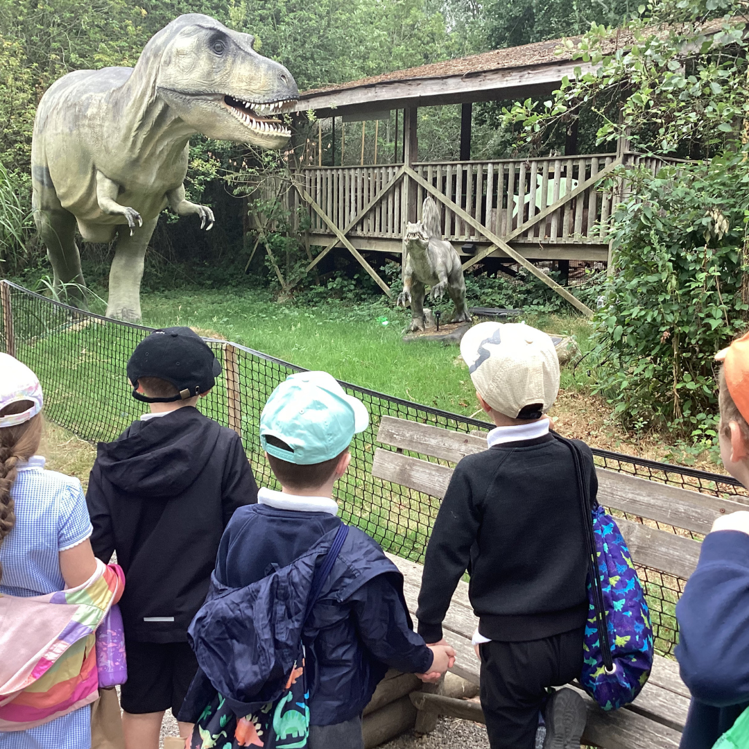 four children looking at a 'dinosaur enclosure' of large model dinosaurs