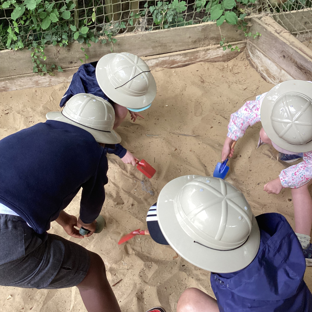 four children in toy hard hats digging in sand for fossils
