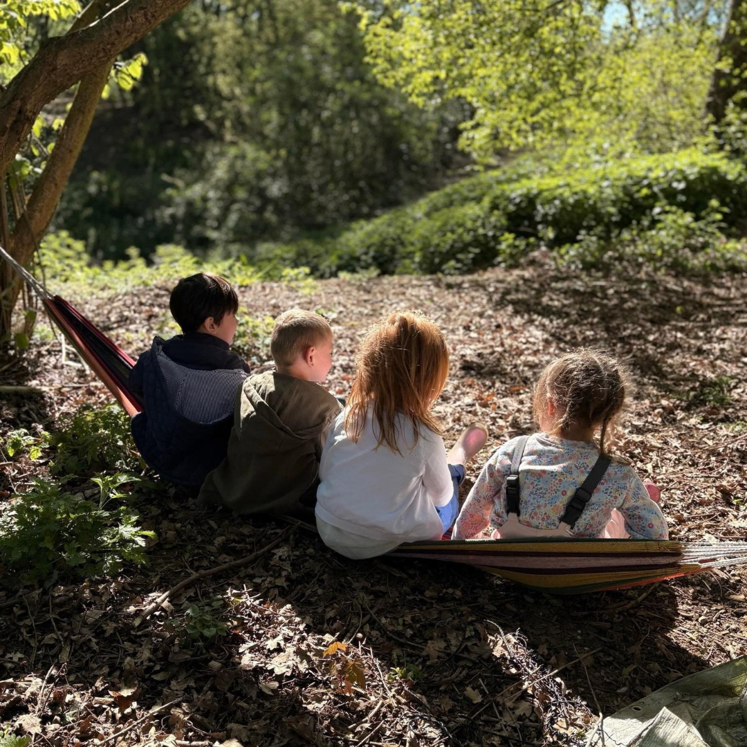four children sitting in the school forest school setting