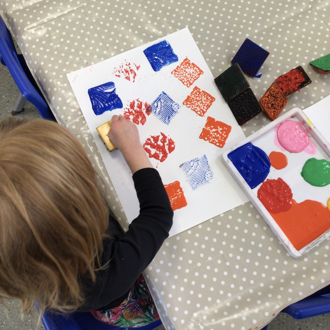 A photo taken from above of a child printing with bright coloured squares on a piece of paper